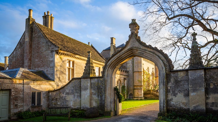 Morning sun shining through a view of the West front through the Gothick arch at Lacock Abbey, Wiltshire